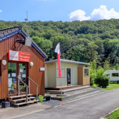 Foto eines Ferienparks mit Rezeption, Flagge, Wohnwagen und Zelten, umgeben von grünen Hügeln.