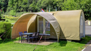 Tenda safari chiamata Coco Sweet con veranda coperta e tavolo all'aperto, immersa nel verde.