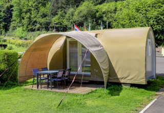 Safari tent called Coco Sweet with a covered outdoor seating area and table, set in a green landscape.