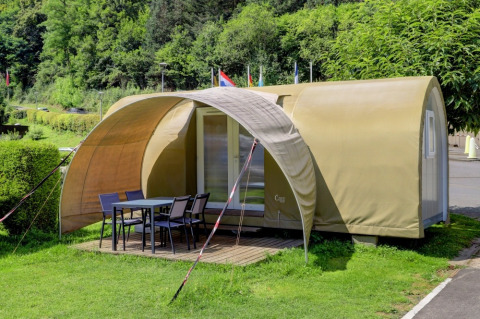 Safari-Zelt namens Coco Sweet mit überdachter Terrasse und Gartenmöbeln in grüner Umgebung.
