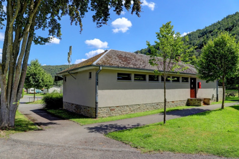 Edificio dei servizi moderno in un villaggio vacanze con glamping, circondato da alberi e paesaggio verdeggiante.
