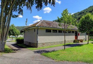Edificio dei servizi moderno in un villaggio vacanze con glamping, circondato da alberi e paesaggio verdeggiante.