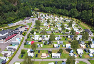Vista aerea di un villaggio vacanze con roulotte, sistemazioni glamping e tanto verde vicino a un bosco.