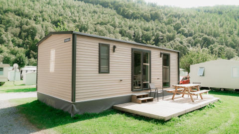 Moderne stacaravan met houten terras en picknicktafel op een glamping vakantiepark tussen groene heuvels.