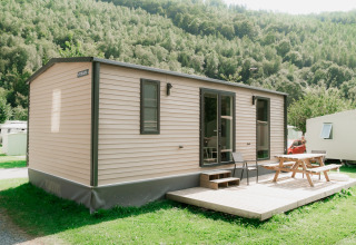 Mobil-home moderne avec terrasse et table de pique-nique dans un parc de glamping entouré de collines vertes.