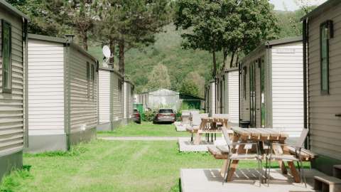 Holiday park glamping area with modern cabins, wooden picnic tables and lush green surroundings.