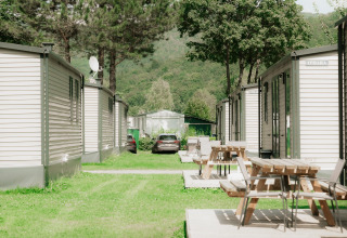 Holiday park glamping area with modern cabins, wooden picnic tables and lush green surroundings.