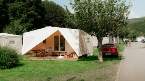Foto van een vakantiepark met glamping-verblijven, witte tenten, picknicktafels en bomen.