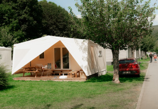 Photo of a holiday park with glamping accommodations, white tents, picnic tables, and green grass.