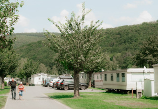 Deux personnes se promènent dans un parc de vacances avec des cabanes de glamping et des collines verdoyantes.