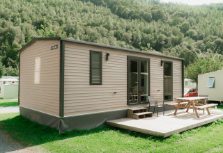 Modern glamping mobile home with terrace and picnic bench at a holiday park surrounded by green hills.