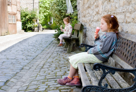 Zwei Mädchen sitzen auf Bänken in einer gepflasterten Straße vor Glamping-Unterkünften und essen Eis.