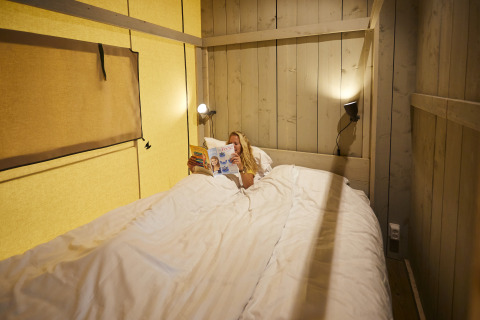 Frau liest eine Zeitschrift im Bett eines Safari-Zeltes bei De Leistert, Niederlande, mit Holzinterieur.