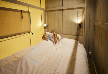 Donna che legge una rivista a letto in una tenda safari accogliente a De Leistert, Paesi Bassi.