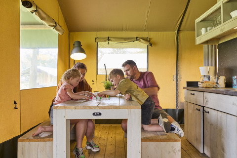 Familie spielt gemeinsam am Tisch in einem Safarizelt bei De Leistert in den Niederlanden.