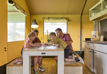 Familie hygger sig ved bordet i en safaritelt på De Leistert, Holland, omgivet af komfort og natur.