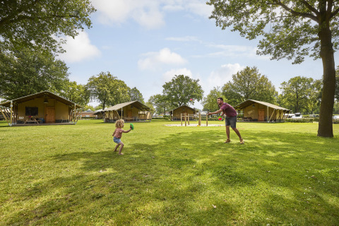 Gezin speelt buiten aan een safaritent bij De Leistert in Nederland, omgeven door gras en bomen.