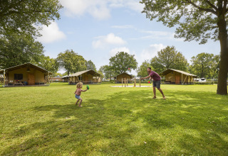 Gezin speelt buiten aan een safaritent bij De Leistert in Nederland, omgeven door gras en bomen.