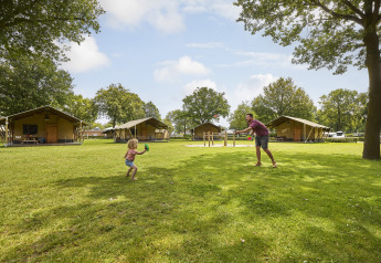 Familia jugando fuera de una tienda safari en De Leistert, Países Bajos, en un entorno verde y arbolado.