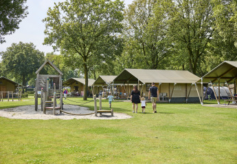 Familia disfruta de un día de camping junto a tiendas safari y parque infantil en De Leistert en Países Bajos.