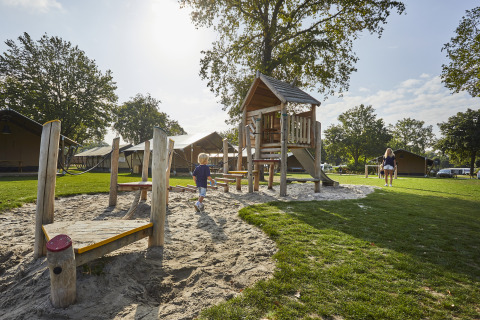 Kinderspielplatz mit Safari-Zelten im Hintergrund im Ferienpark De Leistert, Niederlande, bei Sonne.
