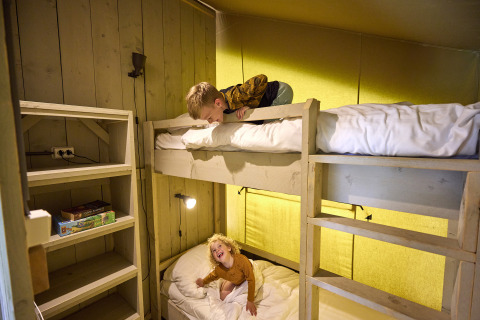 Twee kinderen spelen en lachen op stapelbedden in een safaritent bij De Leistert in Nederland.