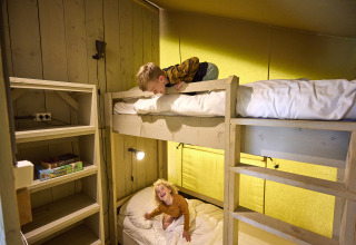 Twee kinderen spelen en lachen op stapelbedden in een safaritent bij De Leistert in Nederland.