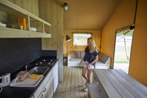 Femme dans une tente safari moderne avec cuisine et salon au De Leistert aux Pays-Bas.
