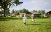 Zwei Kinder spielen auf dem Rasen vor einem Glamping-Zelt im De Leistert in den Niederlanden bei Sonne.