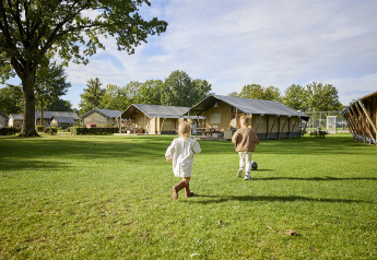 Deux enfants jouent sur la pelouse devant une tente Glamping Comfort à De Leistert, aux Pays-Bas.