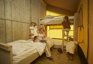 A family enjoys time together in a safari tent with bunk beds and warm yellow light, children playing