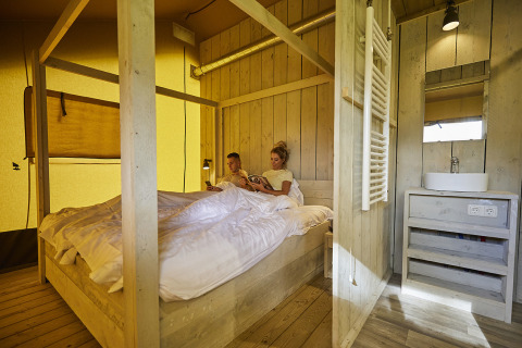 Binnen in een comfortabele glamping tent op De Leistert, Nederland, geniet een koppel ontspannen in bed.