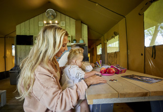 Gezin samen aan een tafel in een Glamping Tent Comfort bij De Leistert in Nederland, puzzelend en knutselend.