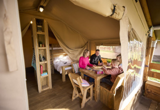 Family playing board games inside a cozy Kalahari Safari tent at De Leistert in the Netherlands, glamping.