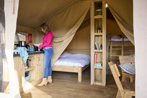 Vrouw kookt in de gezellige safaritent Kalahari Tent bij De Leistert, met bedden en houten meubels.