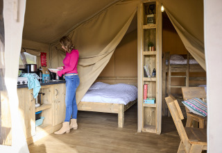 Woman cooking inside the cozy Kalahari Tent safari tent at De Leistert, with beds and wooden furniture.