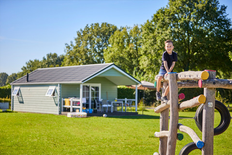 Junge spielt auf einem Klettergerüst vor der Leistert Lodge mit Hütte und Bäumen im Hintergrund.