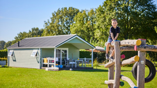 Niño jugando en un trepador frente a Leistert Lodge, con una cabaña moderna y árboles al fondo.