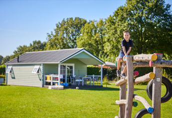 Jongen speelt op klimrek aan Leistert Lodge, met een modern huisje en bomen op de achtergrond.