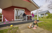 Family enjoys outdoor time in front of a red Leistert Lodge at De Leistert, Netherlands, kids playing.