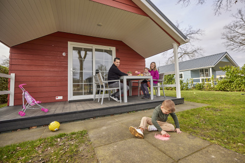 Familie entspannt an einem roten Leistert Lodge bei De Leistert, Niederlande, Kinder spielen draußen.