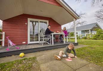 Gezin geniet buiten voor een rode Leistert Lodge bij De Leistert, Nederland, kinderen aan het spelen.