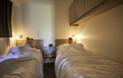 Twee kinderen liggen elk in een apart bed met wit beddengoed in Leistert Lodge, De Leistert, Nederland.