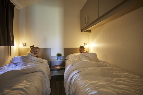 Zwei Kinder liegen in separaten Betten mit weißer Bettwäsche in der Leistert Lodge, De Leistert, Niederlande.