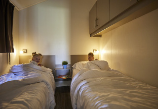 Zwei Kinder liegen in separaten Betten mit weißer Bettwäsche in der Leistert Lodge, De Leistert, Niederlande.