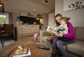 Madre e figlia leggono insieme un libro pop-up nel soggiorno accogliente di Leistert Lodge, De Leistert, Paesi Bassi.
