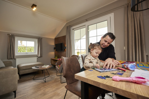 Vader en dochter maken een puzzel samen aan tafel in een warme, sfeervolle Leistert Lodge in Nederland.