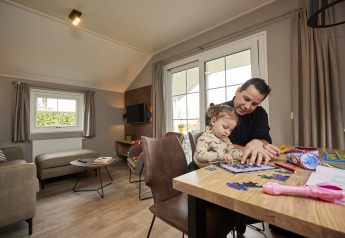 Vader en dochter maken een puzzel samen aan tafel in een warme, sfeervolle Leistert Lodge in Nederland.