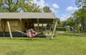 Family relaxing on a hammock in front of a luxury glamping safari tent at De Leistert in the Netherlands.