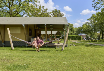 Familie entspannt in einer Hängematte vor einem Glamping-Luxus-Safarizelt im De Leistert, Niederlande.